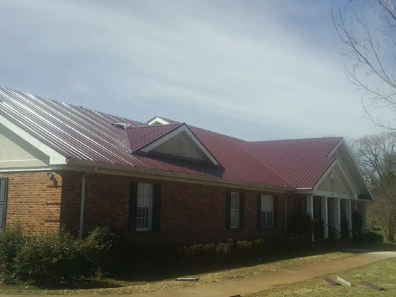 Red metal roof with gabled entries on a long brick building, from a Hail Damage Roof Repair job in Gunnison
