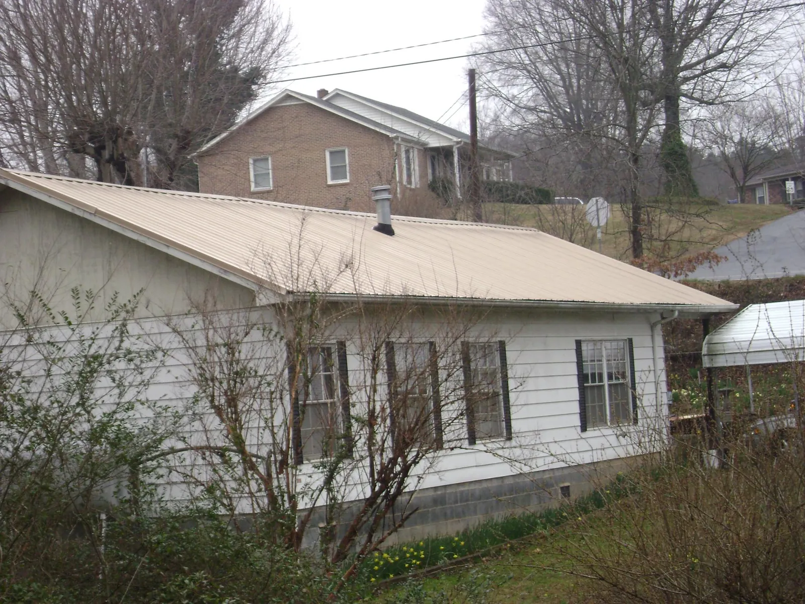 Tan metal roof on a white sided house set into a hillside — Commercial Roofing by Roofing Brothers in Gunnison