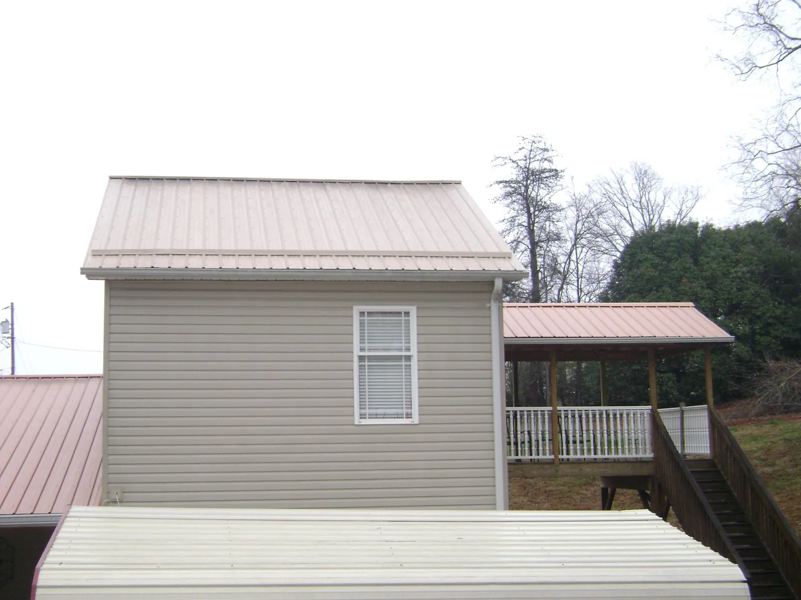 Tan metal roofs on a two story addition and attached porch, from a Roof Replacement job in Gunnison